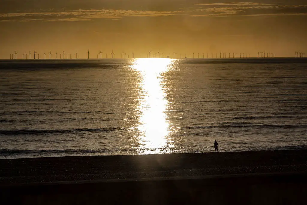 What is Composition in Photography? Lonely silhouetted figure on a beach before sunset. Wind farm on the horizon.