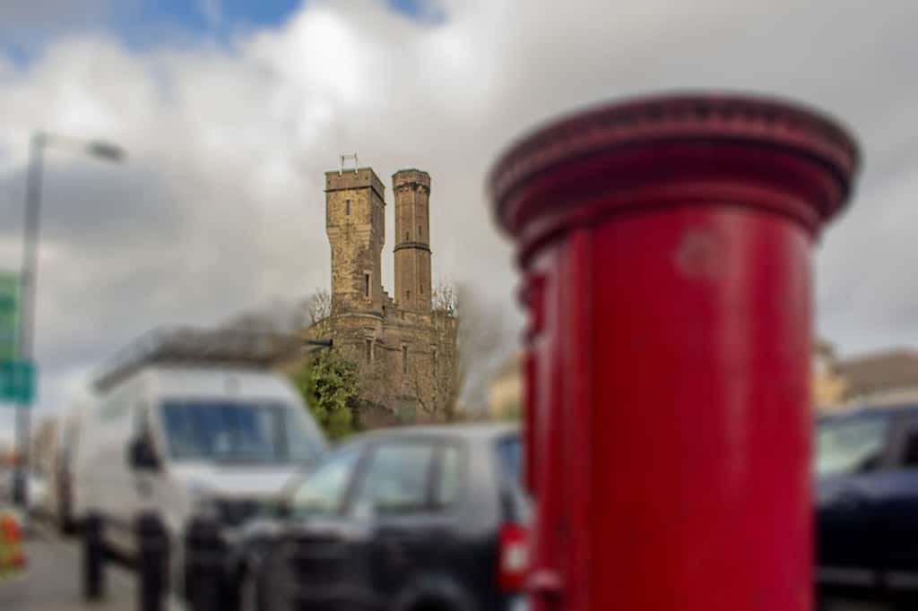 Blurred Red post box in the foreground, blurred parked cars and a sharply focussed castle in the background.