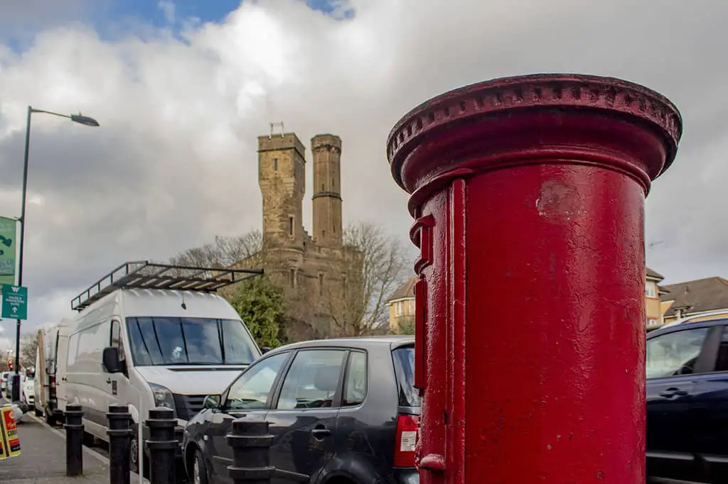 Red post box in the foreground, parked cars and a castle in the background.