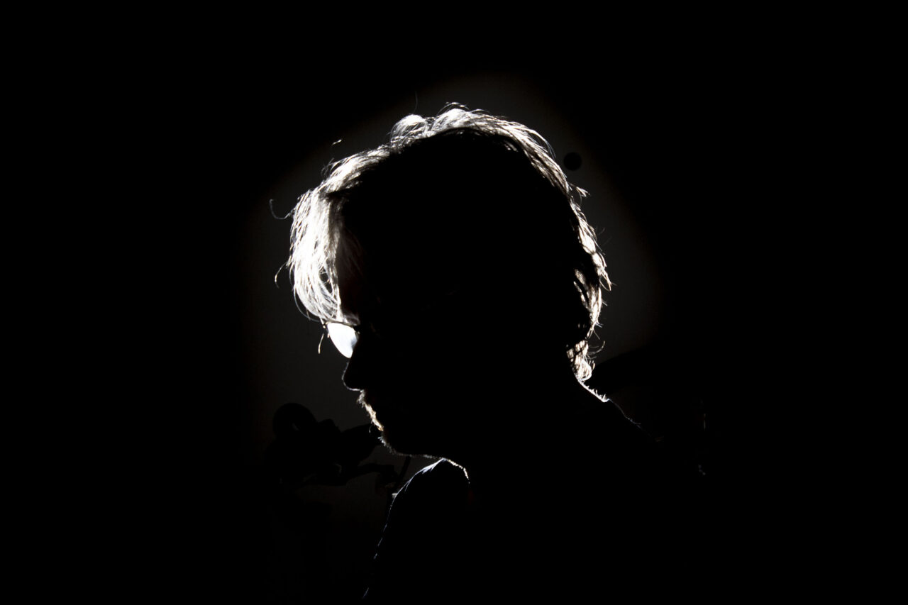 Male subject with fluffy hair lit with a single rear rim light on a black background.