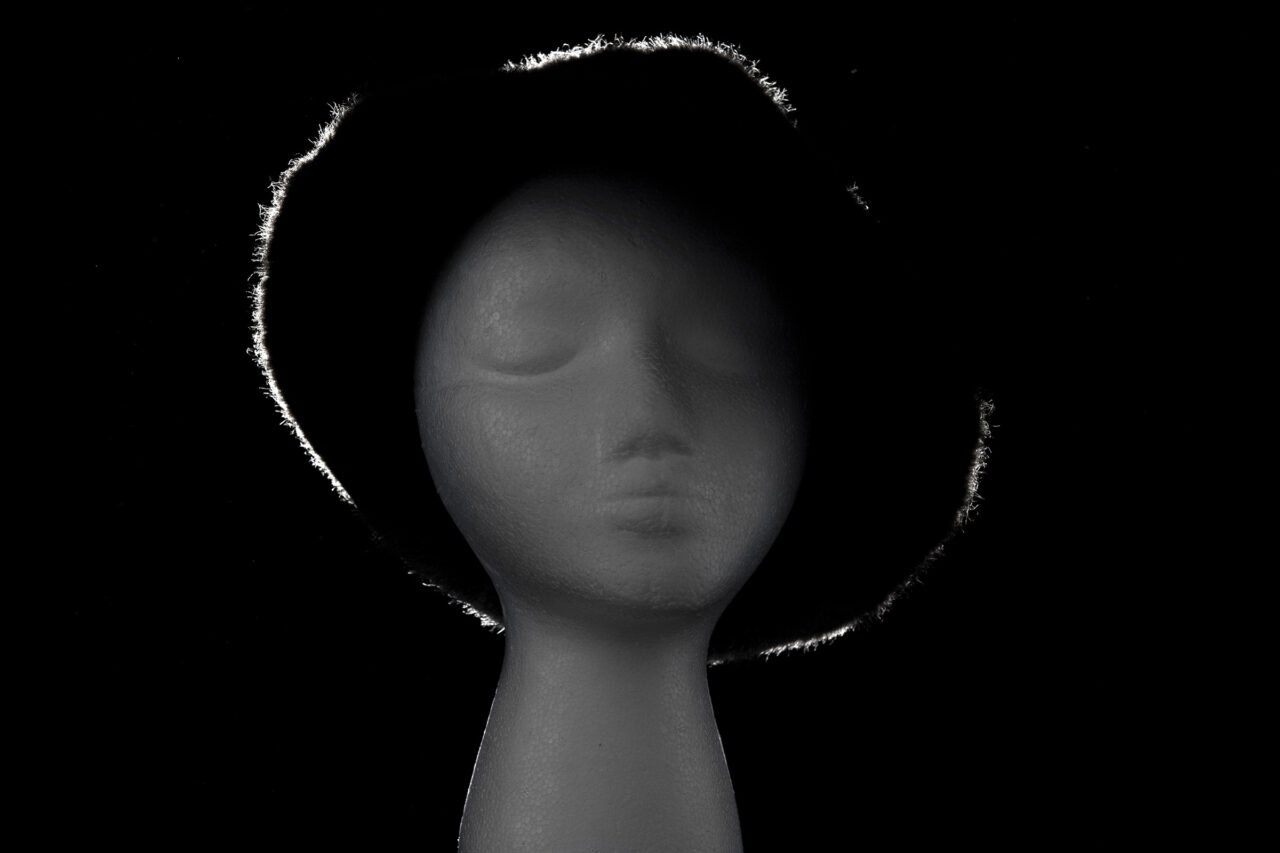 Mannequin head wearing a fur hat lit by a single rear rim light on a black background.