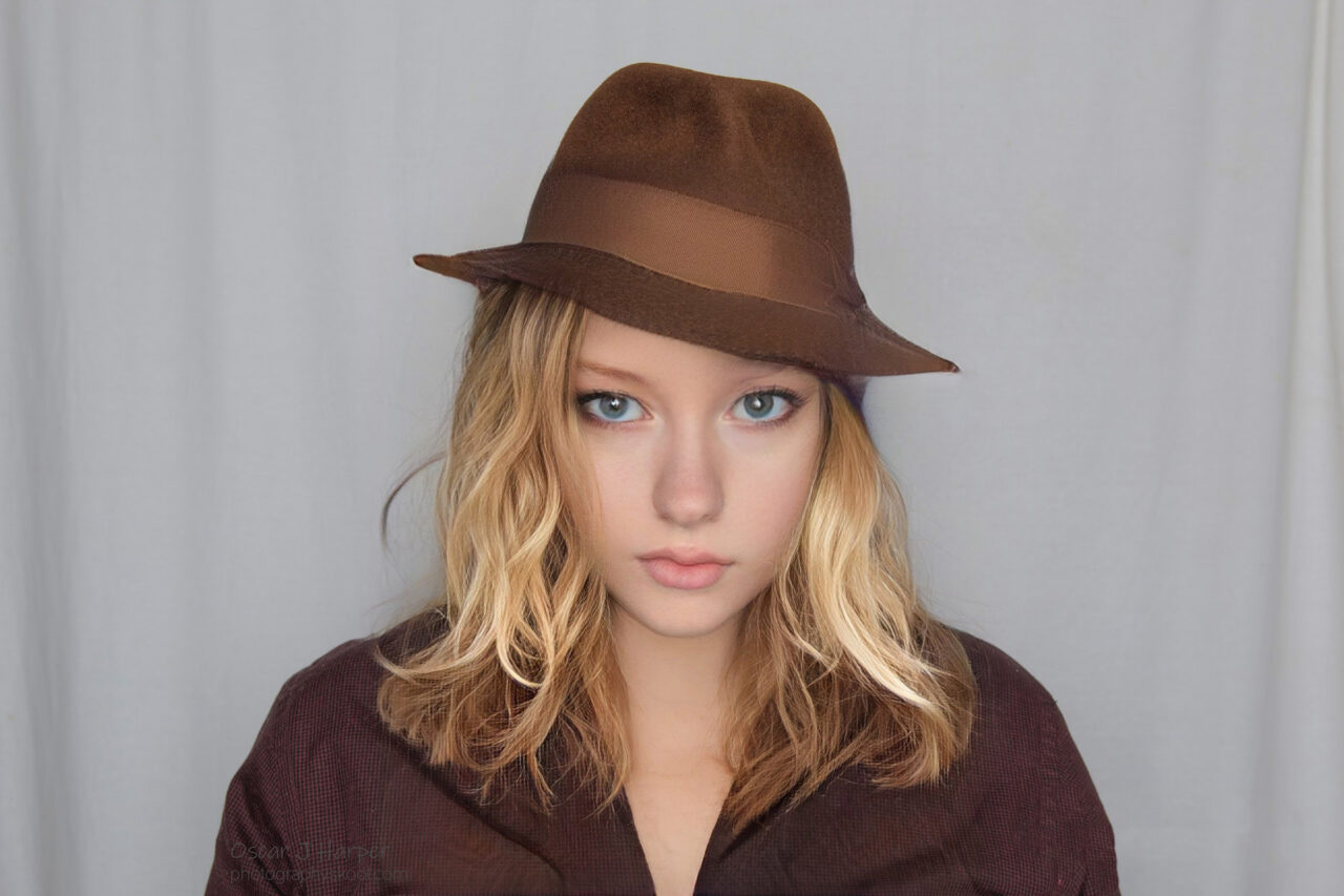 Blond female with long hair and a brown fedora hat lit by shadowless flat studio lighting.
