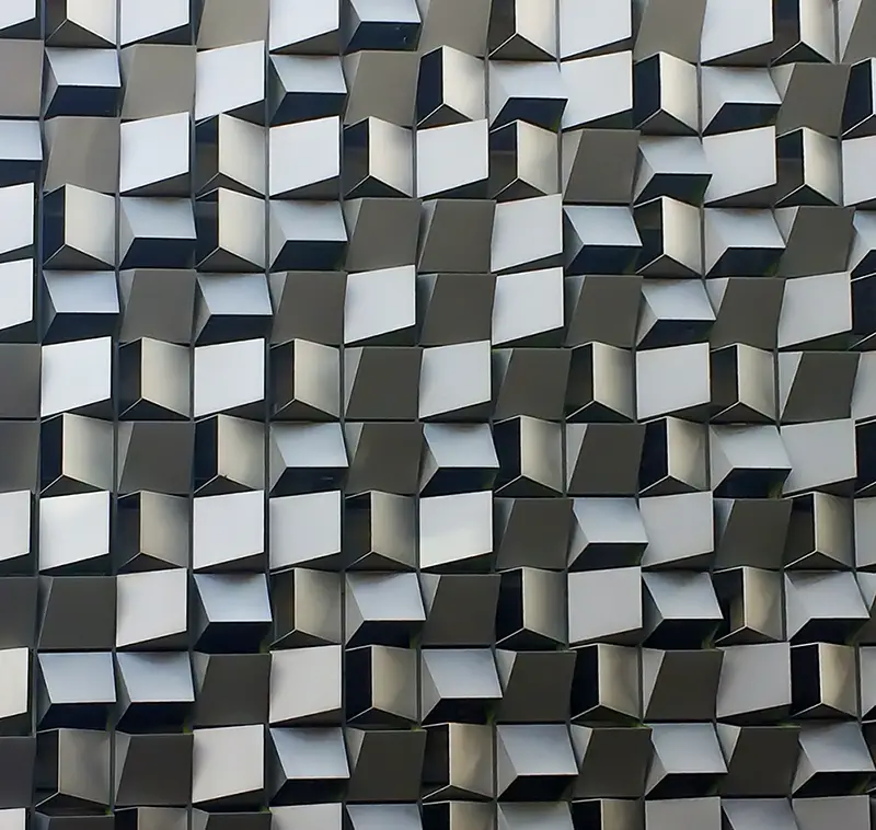 A random pattern of angled metal ventilation cladding panels on the side of a carpark structure.