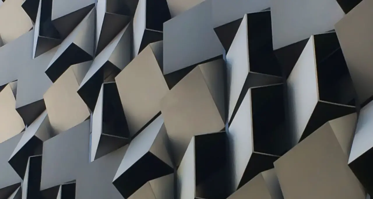 Closeup of a random pattern of angled metal ventilation cladding panels on the side of a carpark structure.