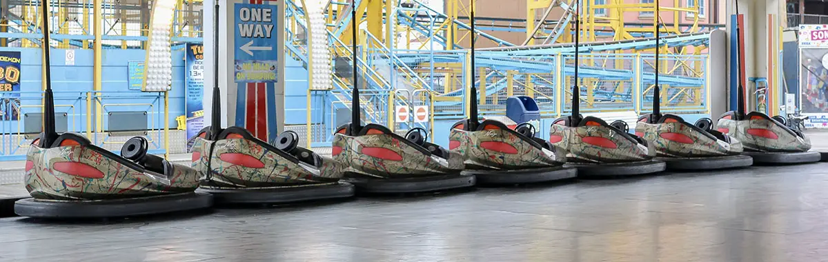 A row of identical bumper cars in a fairground, wildly painted with paint splashes.
