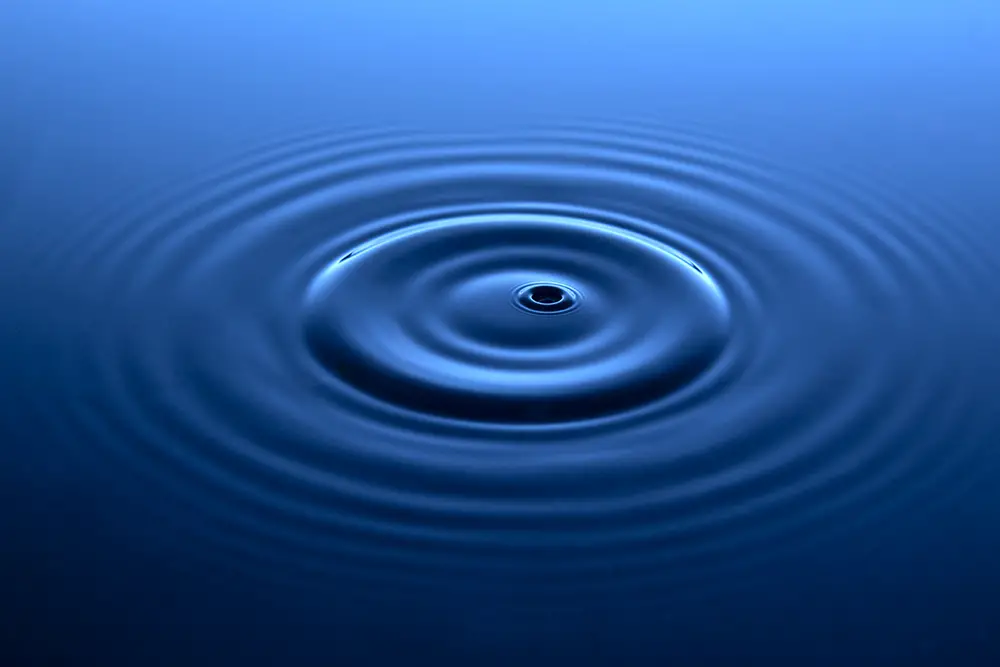 Gentle ripples radiating from a central hole in a deep blue, viscous looking liquid.